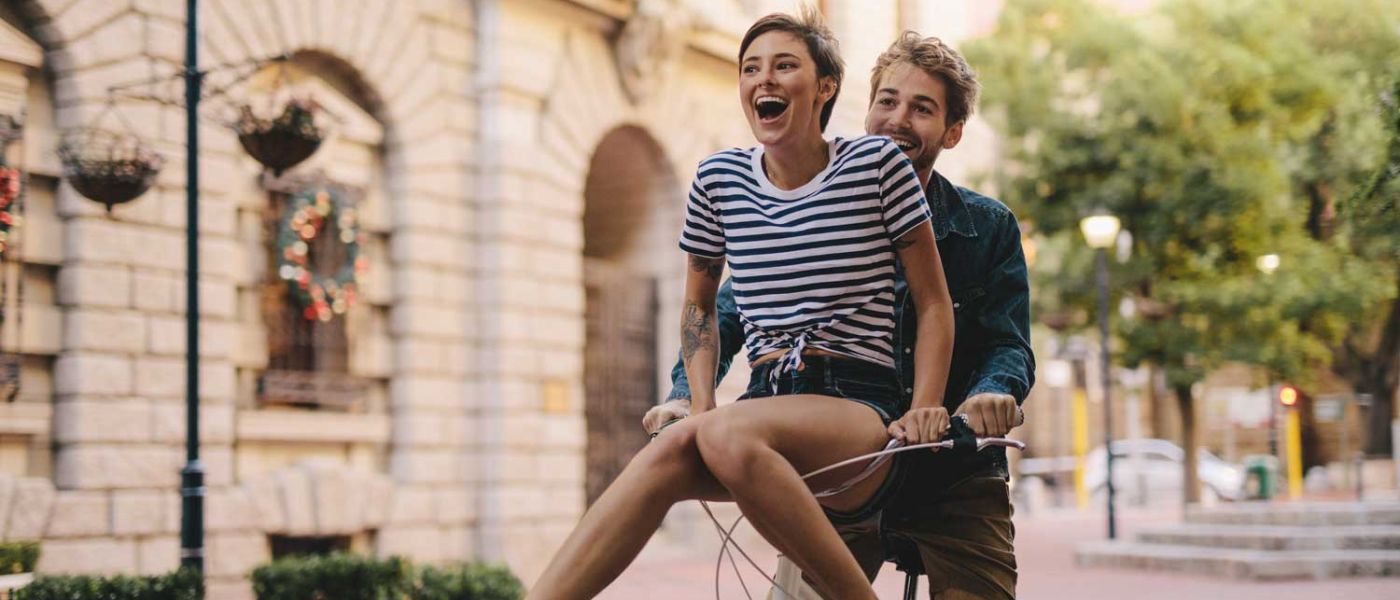 Ein Freundlicher Sommertag. Ein junges Parr sitz auf dem Fahrrad und fährt lachend und glücklich durch die Stadt. 
