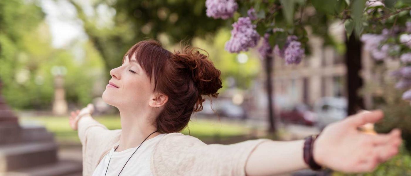 Glückliche Frau mit ausgebreiteten Armen lächelt zufrieden und fühlt sich frei.