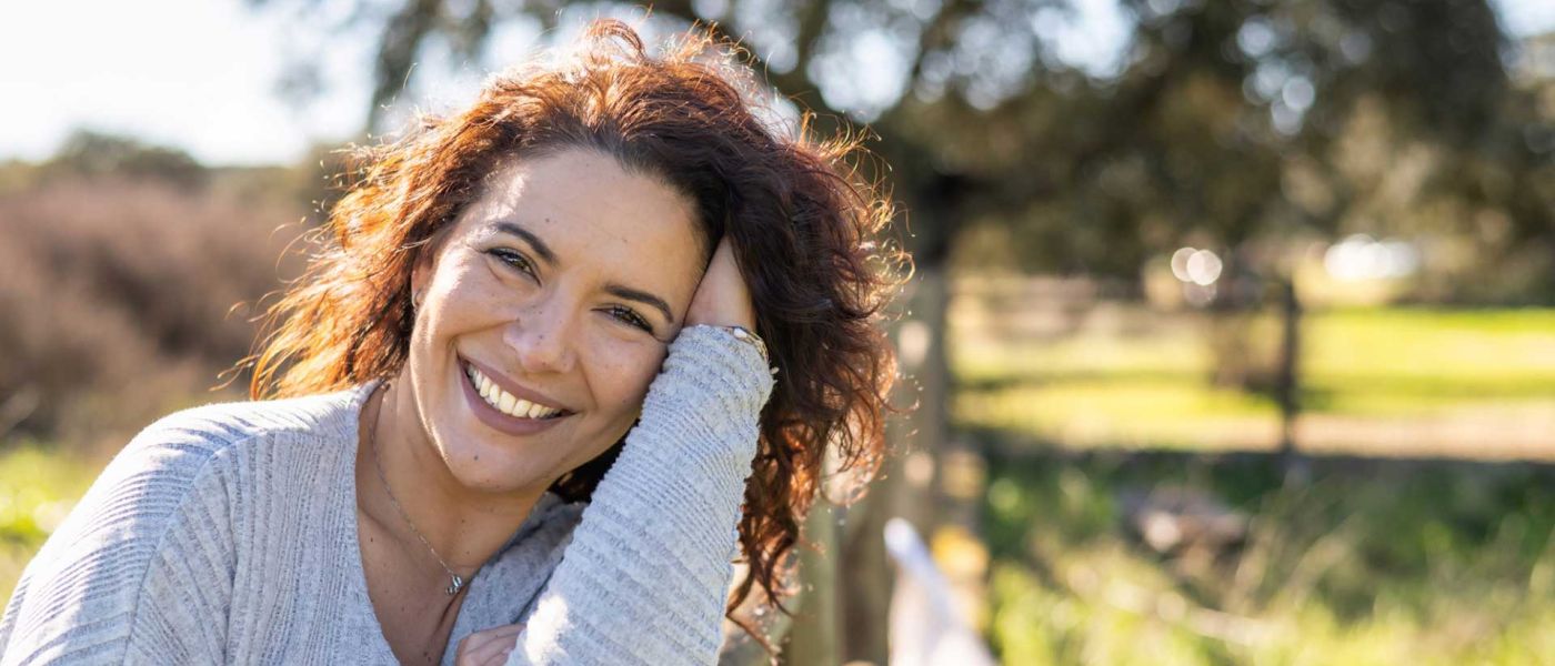 Junge Frau mit baruenen locken lächelt glücklich unf zufrieden.