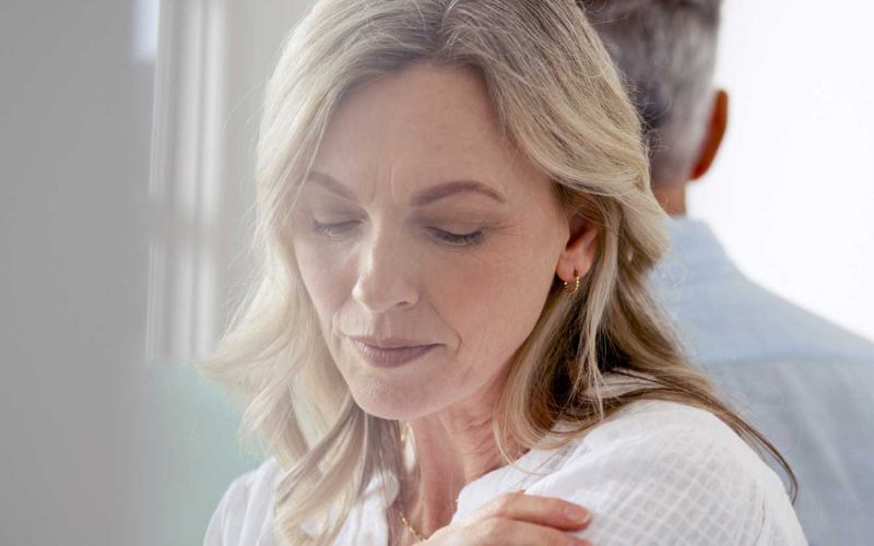 Frau mittleren Alters schaut mit niedergeschlagenen Augen traurig aus. Sie und ihr Partner haben sich von einander abgewendet.