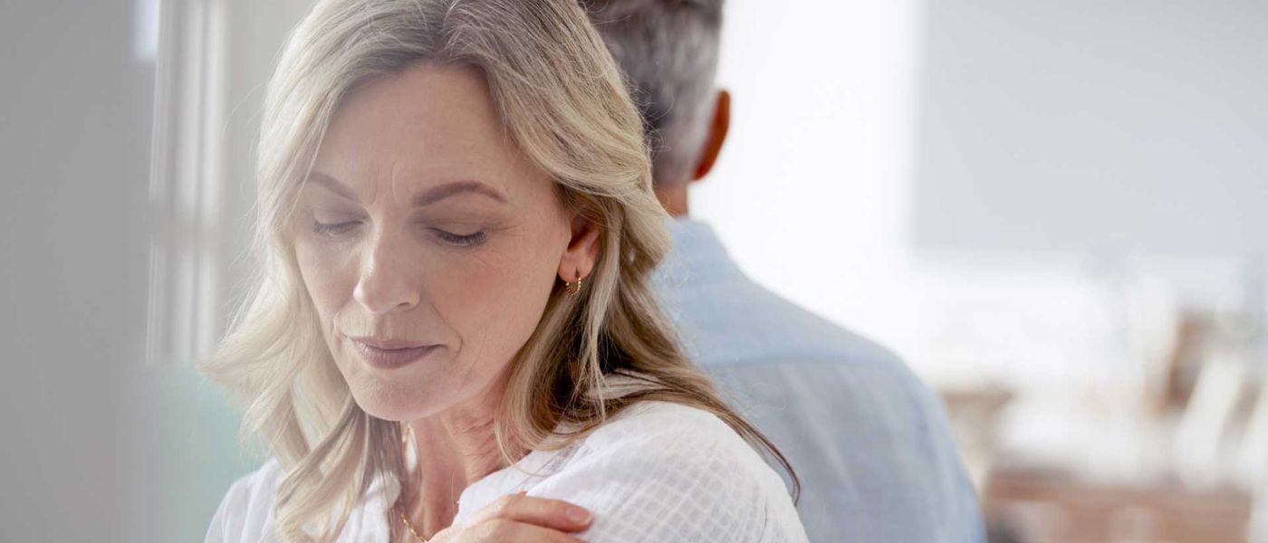 Frau mittleren Alters schaut mit niedergeschlagenen Augen traurig aus. Sie und ihr Partner haben sich von einander abgewendet.